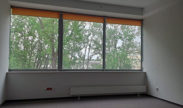 Na ścianie krótszej na wprost na całej szerokości są trzy okna jedno obok drugiego. Są zamontowane w oknach rolety w kolorze pomarańczowym.